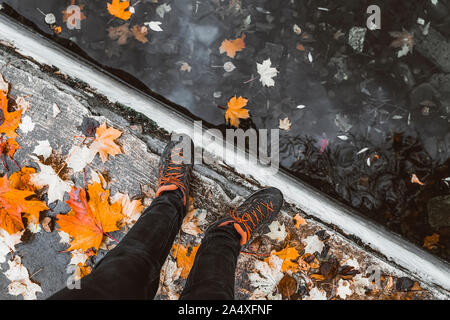 Paar Beine im Sport sneakers neben dem Wasser, die über helle gefallenen Blätter im Herbst. Jahreszeiten, Herbst Spaziergang Stockfoto