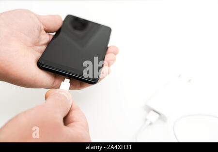 Ein Mann ist das Einfügen eines Netzkabels in den Mini-USB-Kabel für das Aufladen des Smartphones. Stockfoto