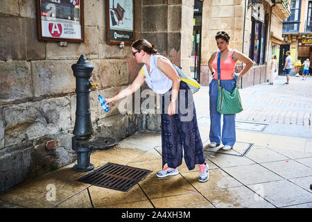 Touristen füllen eine Wasserflasche an einem öffentlichen Trinkwasserbrunnen an einem heißen Tag im Casco Viejo, Bilbao, Spanien Stockfoto
