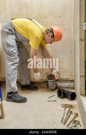 Der Arbeiter ist die Installation einer Kläranlage Abflussrohr an den eingebauten Tank der Wc installieren. Stockfoto