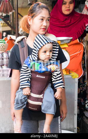 Mae Sot, Thailand - 3. Februar 2019: Frau, die ein Kind in einem Kabelbaum. Babys und Kinder sind meistens um durchgeführt. Stockfoto