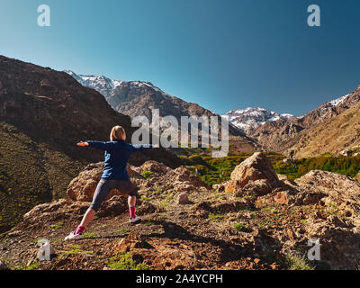 Junge blonde Mädchen übungen Stretching auf dem Berg über dem grünen Tal von Imlil im Hohen Atlas, Marokko Stockfoto