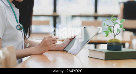 7/8 shot der jungen Ärztin Prüfung Ärztlicher Bericht während der Verwendung von Tablet Stockfoto
