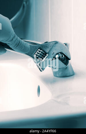 Mann Montage Reparatur auf einem Waschbecken Wasserhahn mit einem verstellbaren Gabelschlüssel tippen. Mit blau Toning Stockfoto