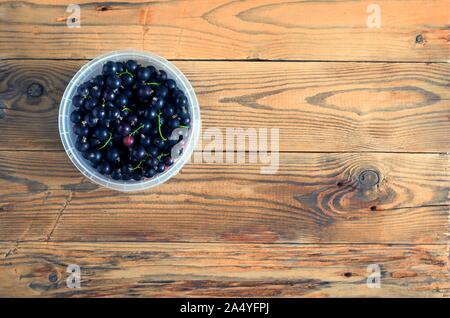 Draufsicht Schwarze Johannisbeere Beeren und Rote Stachelbeeren in einem Kunststoffbehälter auf dem hölzernen Hintergrund. Stockfoto