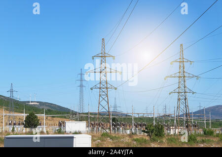 Stromübertragung Pylonen gegen den blauen Himmel. Hochspannung Strommasten mit Windkraftanlagen. Stockfoto