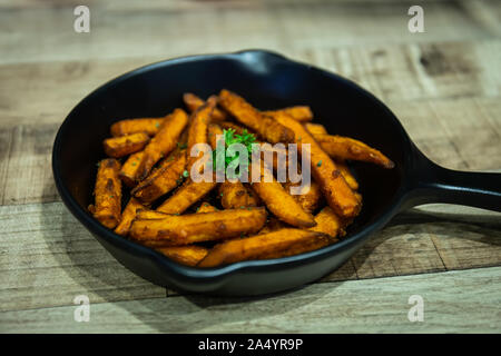 Pommes frites in einer schwarzen Pan ruht auf einem Holztisch auf einer Halloween Party Stockfoto