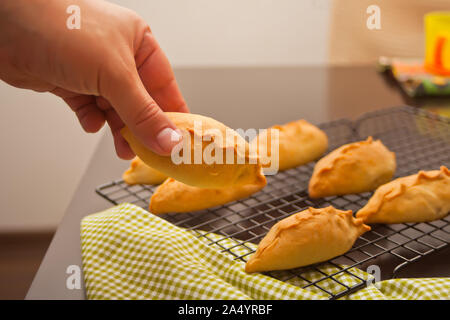 Die Hand des Mannes eine hausgemachte leckere rustikale Backwaren frische Pasteten mit Fleisch und Kartoffeln aus dem Metall backaufsatz nehmen. Stockfoto