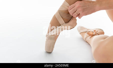 In der Nähe von schönen Beine der jungen Ballerina, die auf Pointe Shoes auf weißem Hintergrund setzt. Ballet Dancer und Praxis Konzept Hintergrund Stockfoto