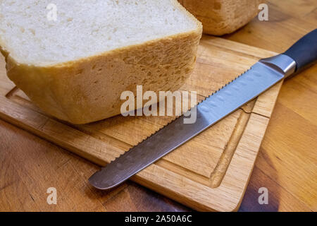 Frisch gebackenes Brot in der Hälfte auf einer Küche aus Holz und liegt neben einem Brot Messer zum Schneiden von Brot. Home Küche. Stockfoto