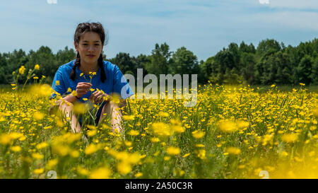 Jugendlich Mädchen im großen Feld mit gelben Blumen und Bäume im Hintergrund sitzen Stockfoto