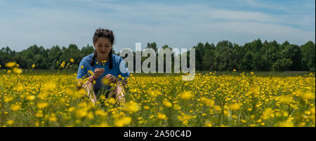 Jugendlich Mädchen mit geschlossenen Augen sitzen im großen Feld mit gelben Blumen und Bäume im Hintergrund Stockfoto