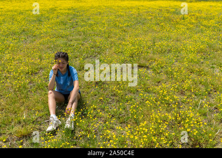 Jugendlich Mädchen mit geschlossenen Augen mit Blumen und sitzen im großen Feld mit gelben Blumen und Bäume im Hintergrund Stockfoto