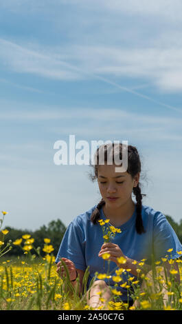 Jugendlich Mädchen mit Blumen und sitzen im großen Feld mit gelben Blumen und Bäume im Hintergrund Stockfoto