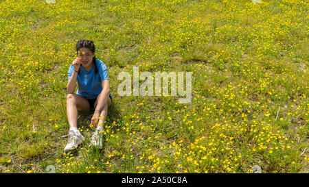 Jugendlich Mädchen mit Blumen und sitzen im großen Feld mit gelben Blumen und Bäume im Hintergrund Stockfoto