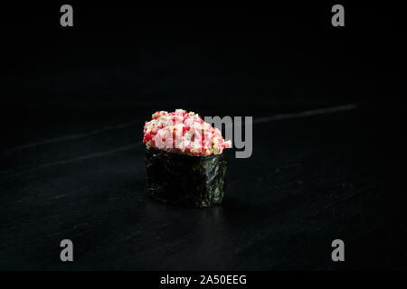 Japanische Küche single gunkan muki Ebi: fein gehackt Riesengarnelen mit Tobiko Kaviar, Avocado in Nori Blatt auf einem schwarzen Hintergrund gewickelt Stockfoto