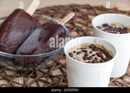 Raw Banane Eis mit Kokosmilch, beschichtet mit natürlichen Schokolade, in einem White Paper Cup, Schokolade und Eis am Stiel auf Sticks in Glasschale. Gesund Stockfoto
