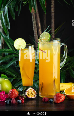 Ananas Mango Cocktail in einer Kanne und Glas auf einem dunklen Hintergrund mit Obst: Ananas, Mango, Erdbeere, Mango Püree, Ananassaft, Pfirsich, Apfel Stockfoto