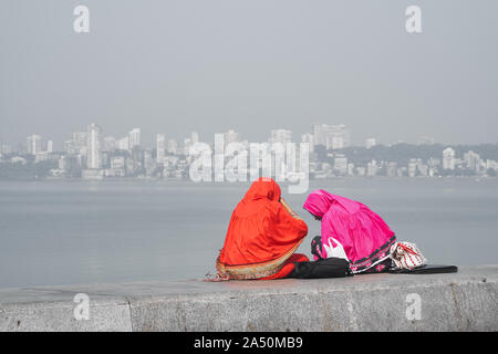 Zwei farbenfroh gekleideten Bohra muslimische Frauen auf dem Uferdamm des Marine Drive, einem Boulevard entlang der Arabischen See in Mumbai (Bombay), Indien sitzen Stockfoto