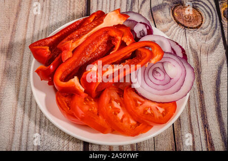 In Scheiben geschnittene Tomaten, Paprika und Zwiebeln in eine Platte auf einem Holztisch Stockfoto