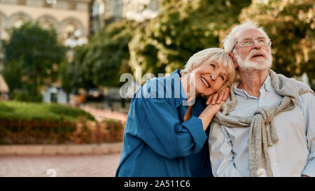 So glücklich zusammen. Portrait von Schöne ältere Frau lehnte sich an die Schulter ihres Mannes und lächelnd, während man im Freien an einem sonnigen Tag Stockfoto