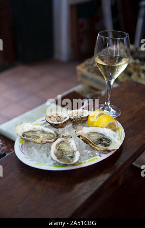 Austern serviert auf Eis mit Zitrone mit einem Glas Champagner oder Weiß/Sekt. Frische Austern Platte auf einem Fischmarkt. Stockfoto