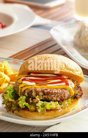 Schönen saftigen Hamburger mit Schnitzel, beträufelt mit Senf, Mayonnaise und Ketchup auf dem Tisch. Pommes frites und Salat. vertikale Bild einer Bur Stockfoto