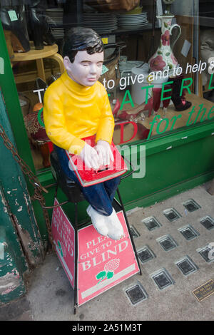 Bitte den Blinden Sammelbox und Abbildung außerhalb einer Charity Shop in Twickenham, London, UK Geben Stockfoto