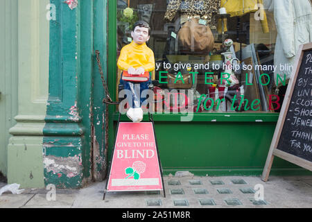 Bitte den Blinden Sammelbox und Abbildung außerhalb einer Charity Shop in Twickenham, London, UK Geben Stockfoto