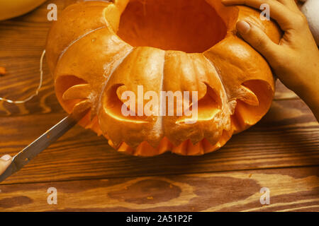 In der Nähe von des Menschen Hand schnitzen Kürbis für Halloween auf Holz rustikal Tisch. Herbst Konzept. Stockfoto