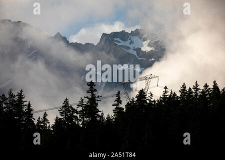 Kontrast zwischen Hochspannungsleitungen und schneebedeckten Gipfeln, hinter sich. Stockfoto