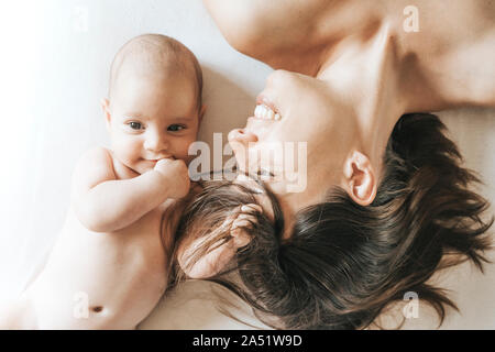 Mutter und Neugeborenem Sohn im Bett gestreckt, der Sohn Fänge Haare der Mutter und sie schaut ihn mit Liebe Stockfoto