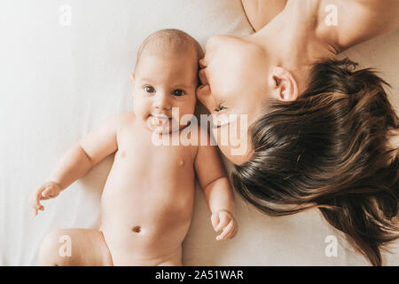 Mutter und Neugeborenem Sohn im Bett gestreckt, Mutter küsst sie Sohn. Das neugeborene Kind ragt die Zunge Stockfoto