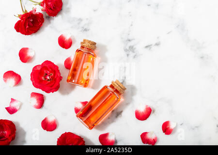 Duftende rose Wasser in Glasflaschen und kleine rote Rosen mit Blüten. Massage, Aromatherapie und Naturkosmetik Konzept Stockfoto