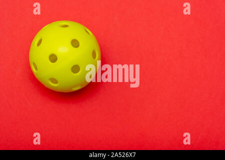 Leuchtend gelbe pickleball oder whiffle Kugel auf einer soliden hellen roten flach Hintergrund symbolisiert Sport und Aktivität mit kopieren. Stockfoto