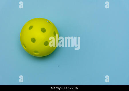 Leuchtend gelbe pickleball oder whiffle Kugel auf einer soliden aqua blau flach Hintergrund symbolisiert Sport und Aktivität mit kopieren. Stockfoto