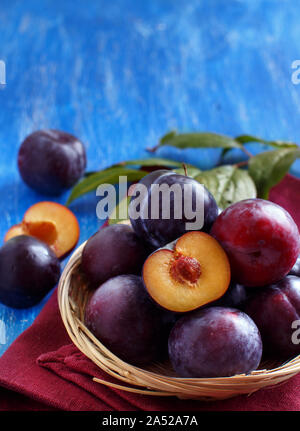 Frische Pflaumen mit Blätter auf einem blauen Holztisch Nahaufnahme Stockfoto