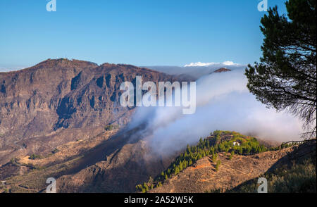 Gran Canaria, Oktober, Wolken fließen in Caldera de Tejeda von rechts über bergpass Cruz De Tejeda, Los Moriscos Klippen von wildfir Stockfoto