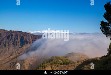 Gran Canaria, Oktober, Wolken fließen in Caldera de Tejeda von rechts über bergpass Cruz De Tejeda, Los Moriscos Klippen von wildfir Stockfoto