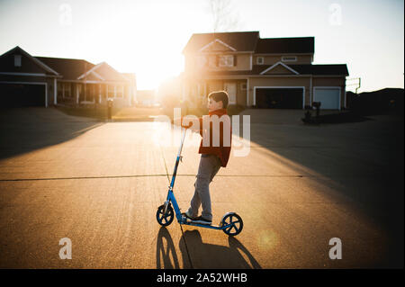 Junge, 7-8 Jahre alt, rollerfahren in der Nachbarschaft in hübsches Licht Stockfoto