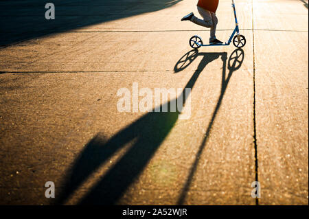 Die untere Hälfte des Jungen, Rollerfahren schnell im Sonnenlicht mit Schatten in der Straße Stockfoto