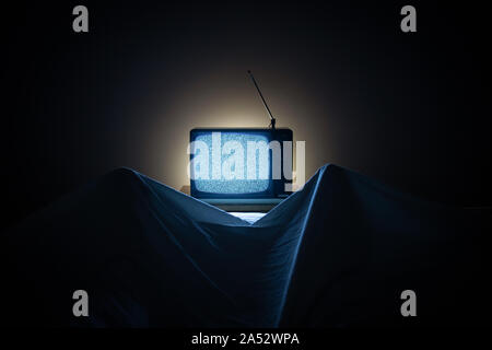 Eine Person schaut in der Nacht in seinem Bett mit seinen Füßen Balg der Blätter. Der TV-Bildschirm ist mit kein Signal und körnige Rauschen Wirkung. Retro TV Stockfoto