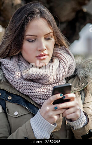 Junge Frau, indem Sie auf eine Zelle Telefon im Winter Sonne Stockfoto