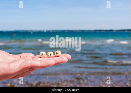 Hand mit Öffnen Sie Palm auf dem Hintergrund des Meeres. Die Buchstaben auf dem Würfel sind komplex in das Wort MEER Stockfoto