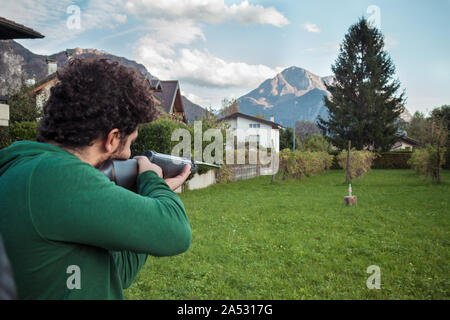 Mann da Übung mit einem Gewehr, Outdoor Sport mit grünem Rasen weit weg zu schießen gibt es ein Ziel Stockfoto