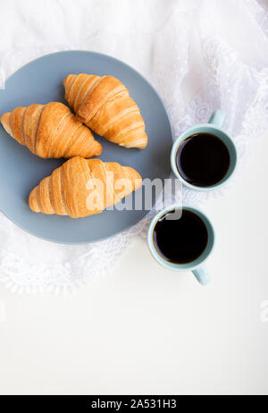 Zwei Tassen Kaffee und Croissants auf dem Hintergrund der Schnürsenkel auf weißem Hintergrund Stockfoto