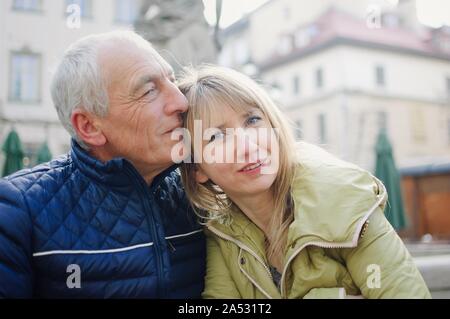 Gut aussehender älterer Mann begrüßt seine junge blonde Frau Ausgabe Zeit zusammen im Freien in der antiken Stadt im frühen Frühjahr oder Herbst. Stockfoto