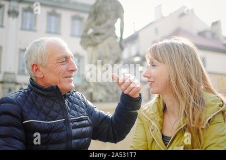 Gut aussehender älterer Mann begrüßt seine junge blonde Frau Ausgabe Zeit zusammen im Freien in der antiken Stadt im frühen Frühjahr oder Herbst. Stockfoto
