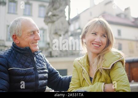 Gut aussehender älterer Mann begrüßt seine junge blonde Frau Ausgabe Zeit zusammen im Freien in der antiken Stadt im frühen Frühjahr oder Herbst. Stockfoto