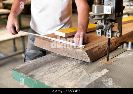 Tischler oder Schreiner Messungen mit einem Maßband aus einem großen Holzbrett in der Holzbearbeitung Workshop in einer Nahaufnahme auf seinen Händen Stockfoto